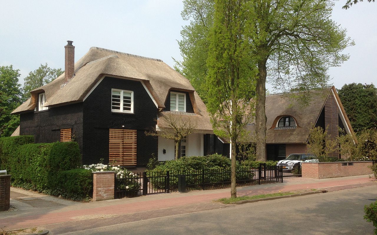 Landelijke woning met rieten dak en zwarte houten gevel.